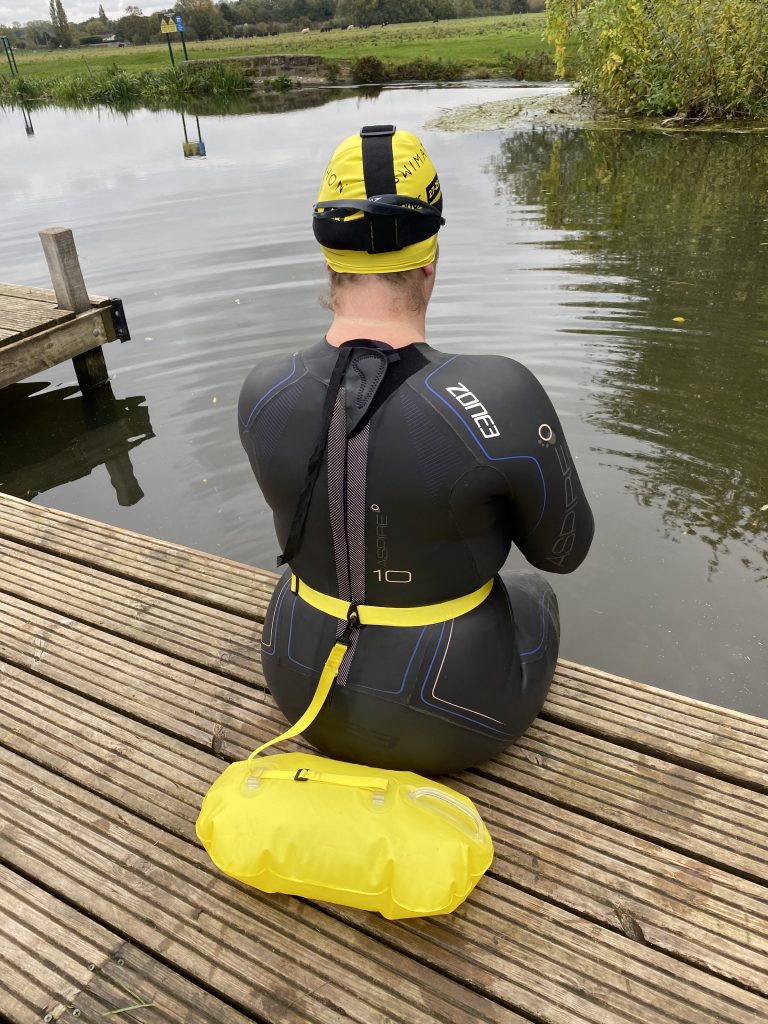 A women sitting on the edhe of a jetty at the side of the river in a wetsuit