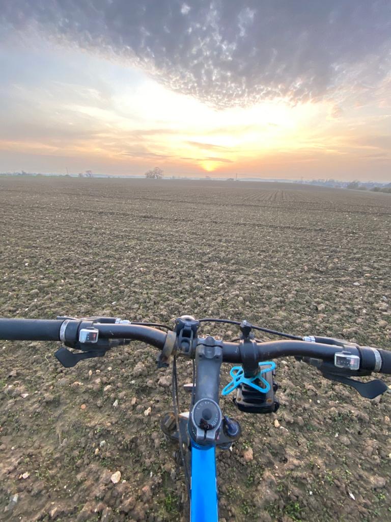 A beautiful sunset over a ploughed field, with bicycle handlebars in the foreground taken from the riders perspective